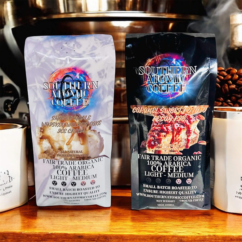 Two Southern Atomic Coffee bags stand upright on a table. One is the Caramel Sweet Potato Pecan Pie and the other is the Smoked Maple Whiskey Walnut Cake Ice Cream blend, both clearly showing their labels.